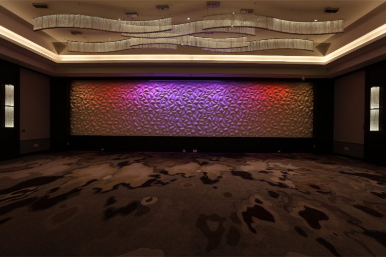 LED linear cove lighting accenting architectural ceiling elements in a hotel lobby and colorful LED lighting highlighting textural modern artwork. Boca Lighting and Controls