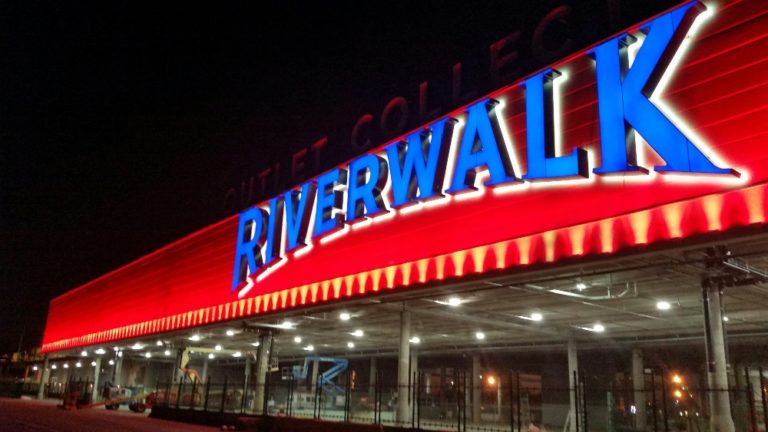 Red LED lighting creates a wash of color on an outdoor Riverwalk sign, while white LED lights create a back light for the blue Boardwalk lettering. Boca Lighting and Controls