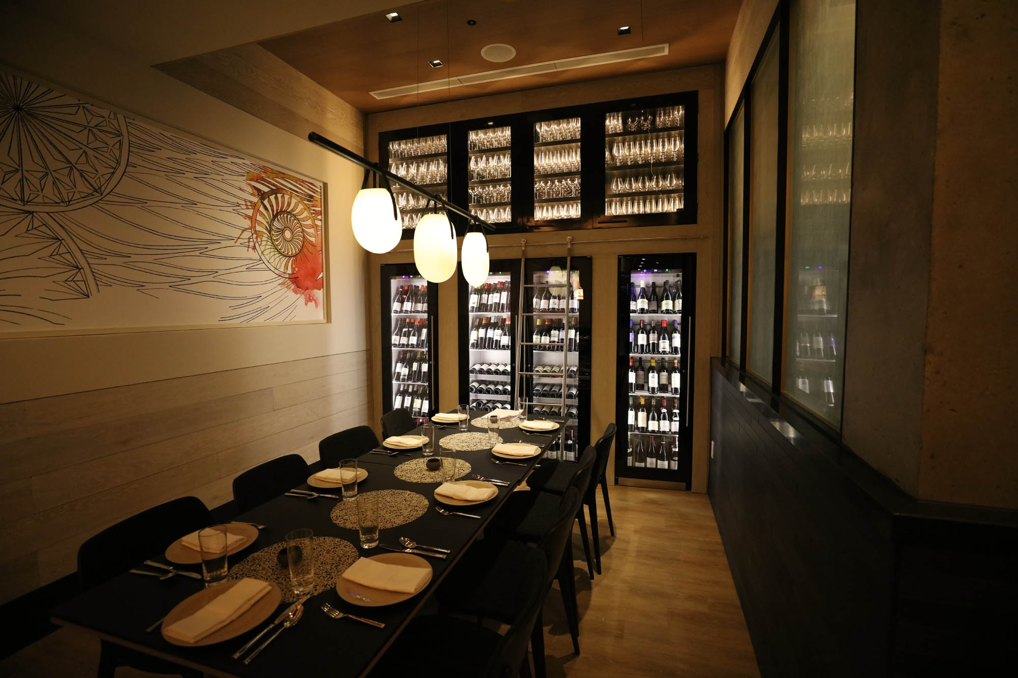 LED strip lights illuminating a wall of glass display shelving for barware and wine coolers in a hotel private dining room. Boca Lighting and Controls
